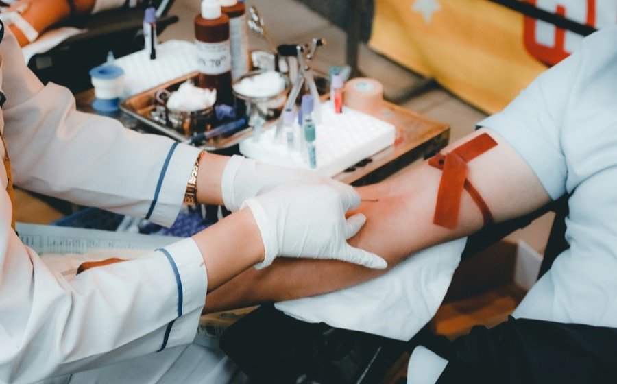 A gloved health worker collecting a blood sample from a patient&rsquo;s arm